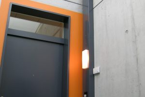 modern interior door with wall-mounted light fixture and concrete wall